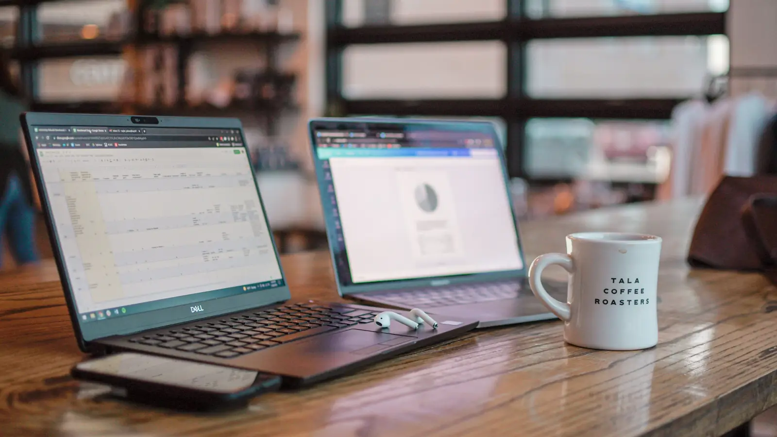 Two open laptops and a mug on a café table