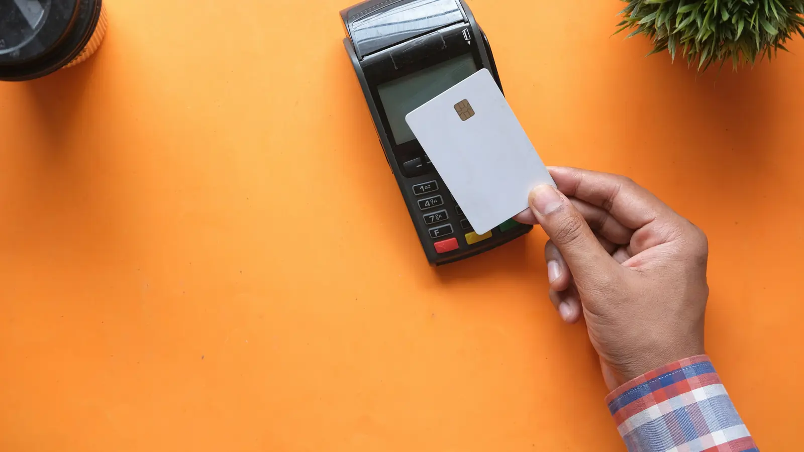 A hand holding a plain card next to a card payment terminal