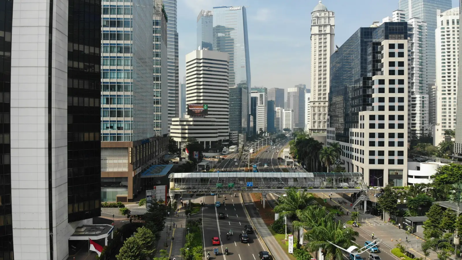 A multi-lane avenue with a pedestrian bridge among office towers in Jakarta