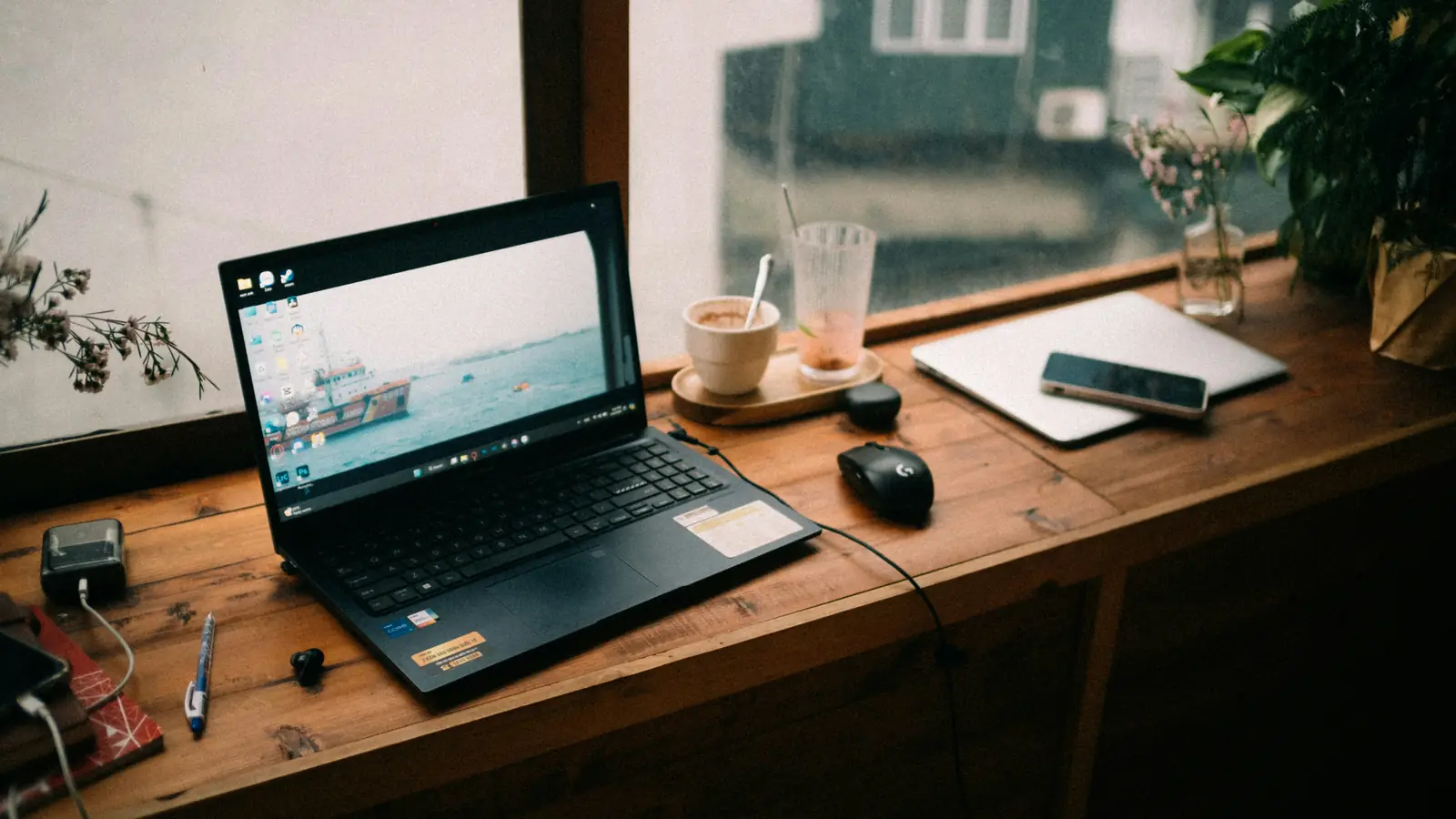 A laptop and a cup of coffee on a wooden desk by a window