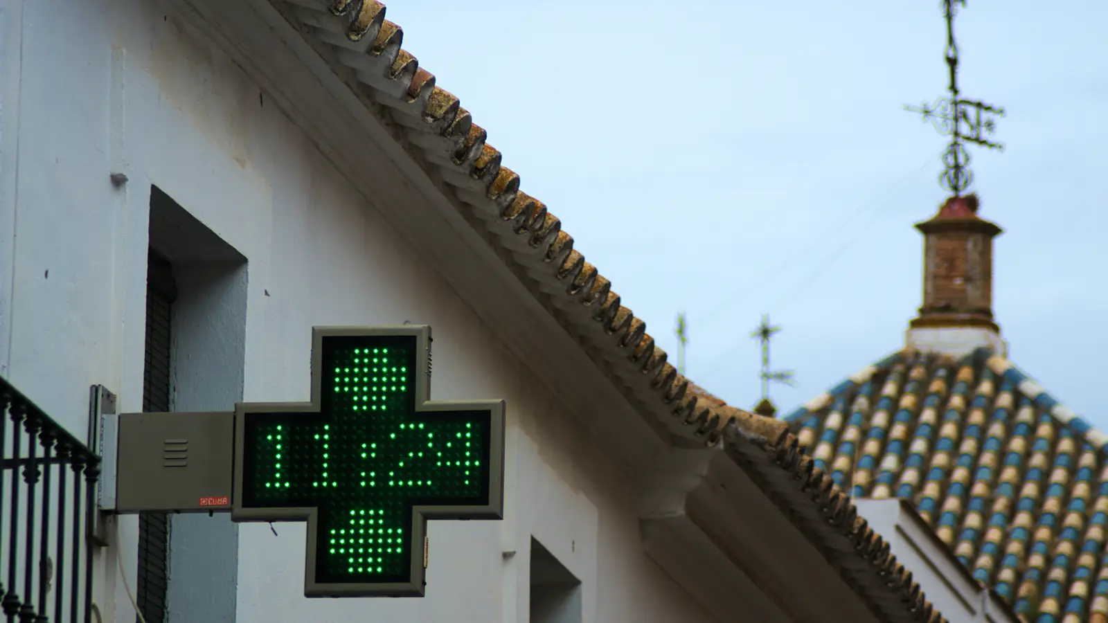 A green pharmacy cross showing the time on a white building